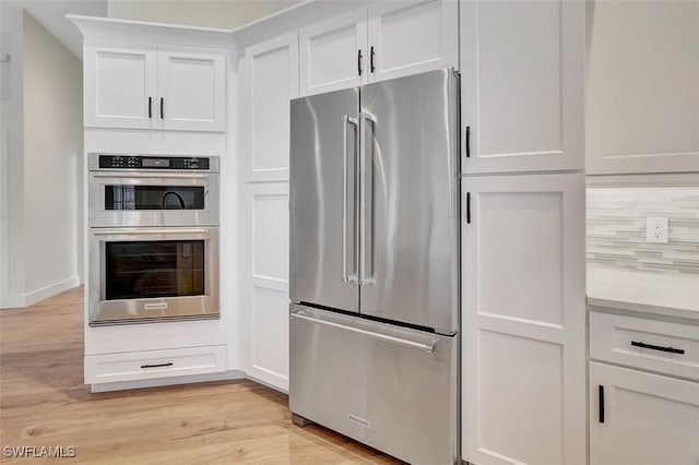 kitchen with light wood-style flooring, tasteful backsplash, appliances with stainless steel finishes, and white cabinets