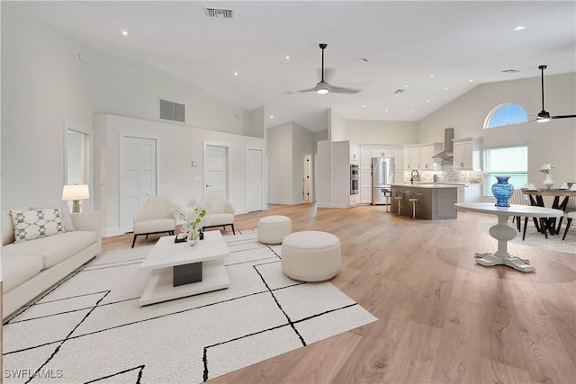 living room featuring light wood-type flooring, ceiling fan, high vaulted ceiling, and sink