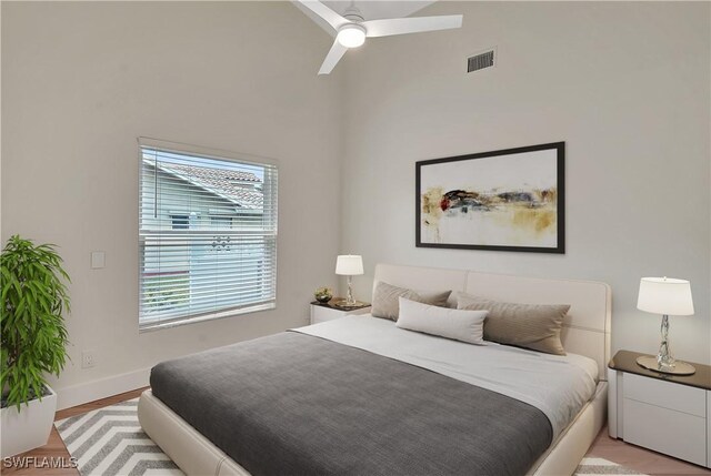 bedroom featuring ceiling fan, multiple windows, light hardwood / wood-style flooring, and a towering ceiling