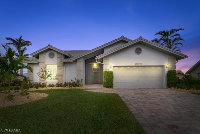 view of front facade featuring stucco siding, an attached garage, a yard, and driveway