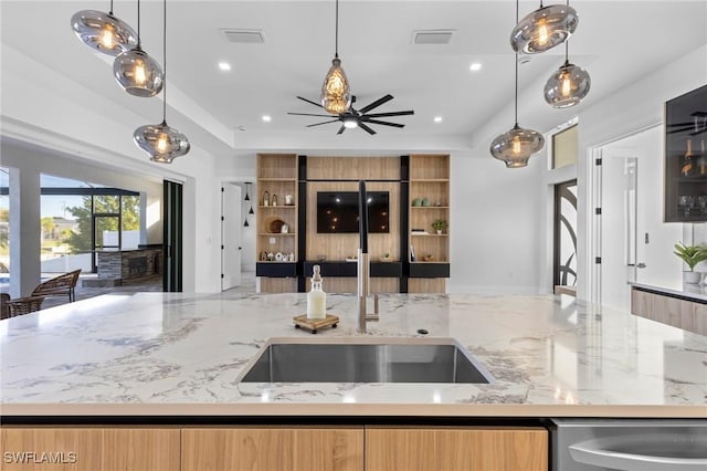 kitchen with sink, light stone countertops, light brown cabinetry, stainless steel dishwasher, and a raised ceiling