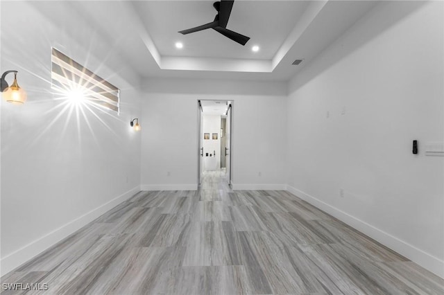 spare room with light wood-type flooring, ceiling fan, and a tray ceiling