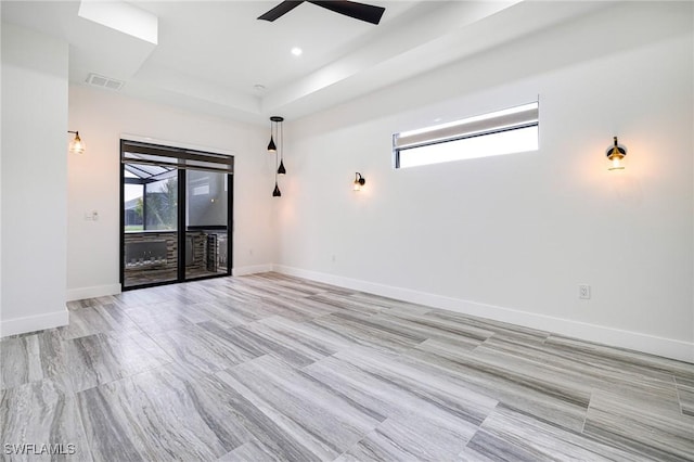 empty room featuring ceiling fan, a tray ceiling, and a wealth of natural light