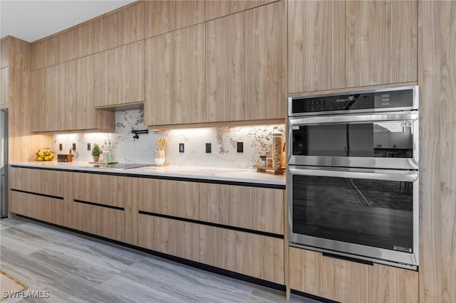 kitchen with double oven, black electric stovetop, light brown cabinets, decorative backsplash, and light wood-type flooring