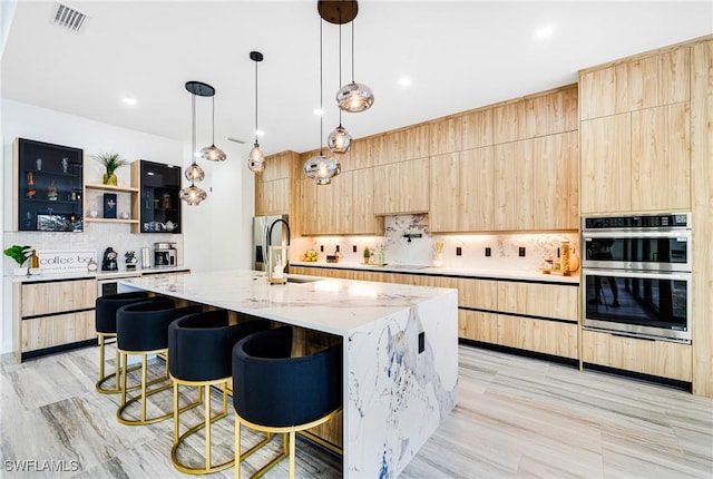 kitchen with hanging light fixtures, light stone countertops, light brown cabinetry, and a spacious island