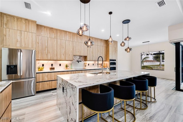 kitchen featuring stainless steel appliances, sink, light stone countertops, and a kitchen island with sink