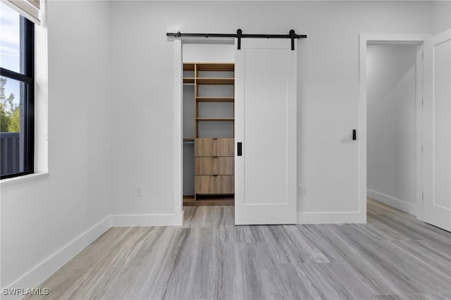 unfurnished bedroom with multiple windows, a barn door, a spacious closet, and a closet