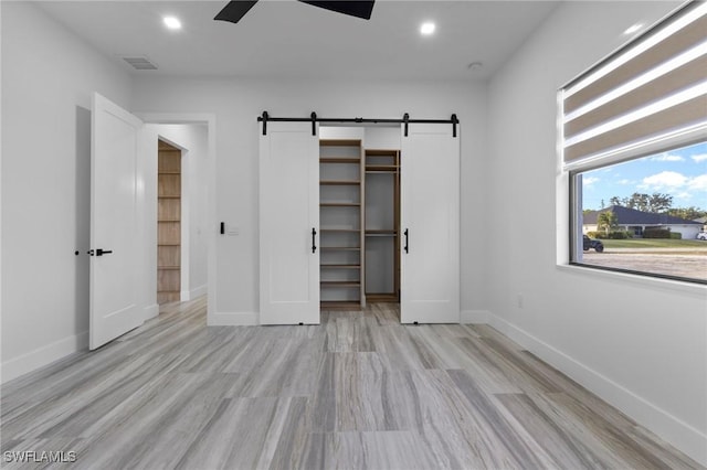 unfurnished bedroom featuring ceiling fan, light hardwood / wood-style floors, a barn door, a walk in closet, and a closet