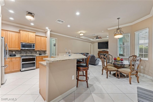 kitchen with light stone countertops, appliances with stainless steel finishes, a kitchen island with sink, ceiling fan, and crown molding