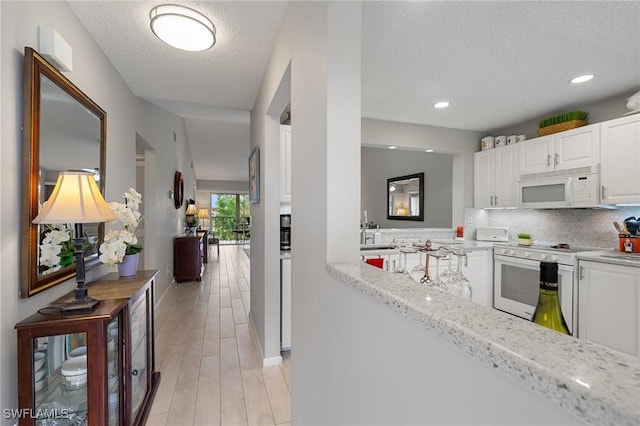 kitchen with white appliances, white cabinets, a textured ceiling, decorative backsplash, and light stone counters