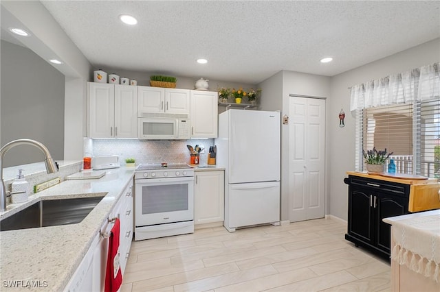 kitchen with sink, white cabinets, light stone counters, white appliances, and a textured ceiling