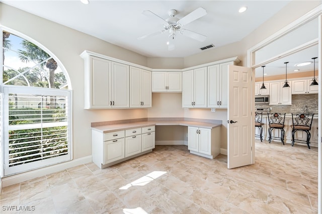 kitchen with built in desk, backsplash, white cabinets, hanging light fixtures, and ceiling fan