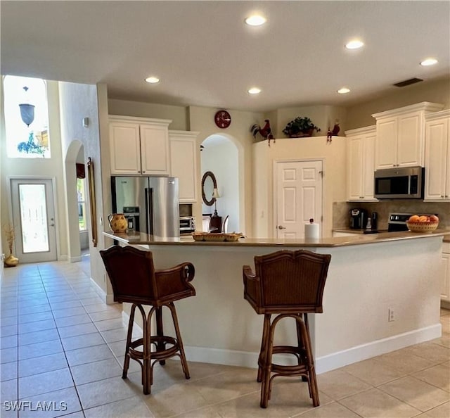 kitchen featuring white cabinets, a large island with sink, appliances with stainless steel finishes, and light tile patterned floors