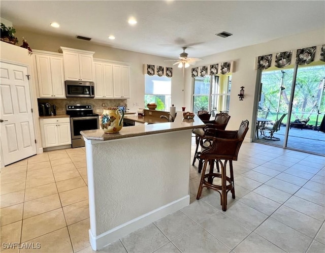 kitchen with ceiling fan, light tile patterned floors, a kitchen island with sink, appliances with stainless steel finishes, and white cabinets