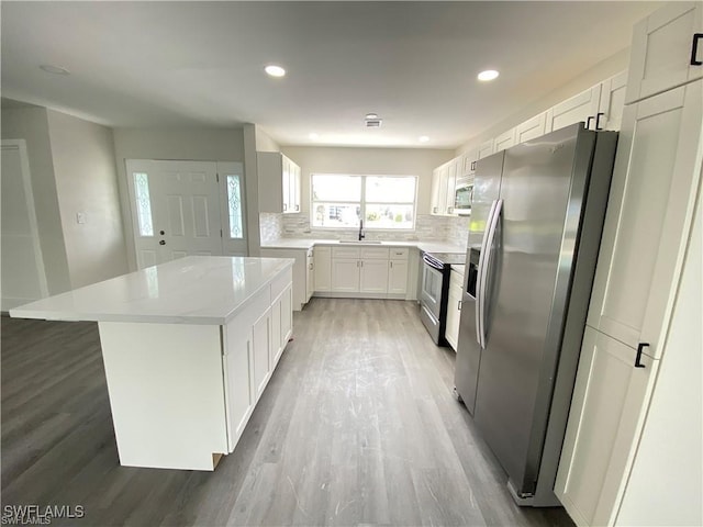 kitchen with appliances with stainless steel finishes, a kitchen island, white cabinetry, tasteful backsplash, and sink