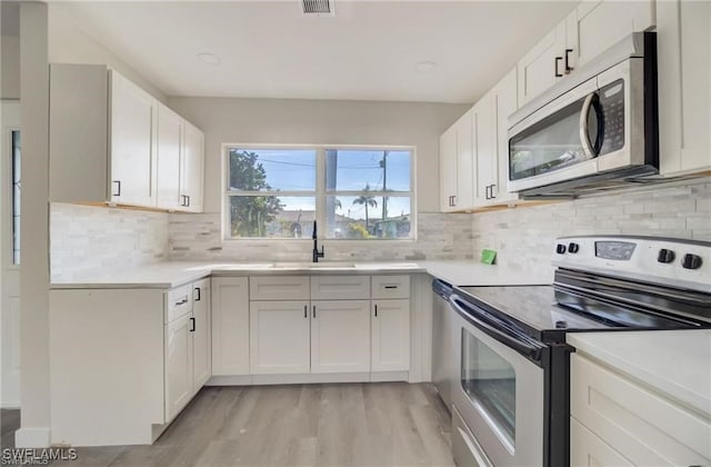 kitchen with light hardwood / wood-style flooring, appliances with stainless steel finishes, sink, white cabinets, and tasteful backsplash