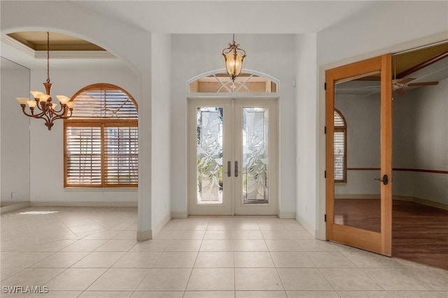 tiled foyer with a chandelier, french doors, ornamental molding, and baseboards