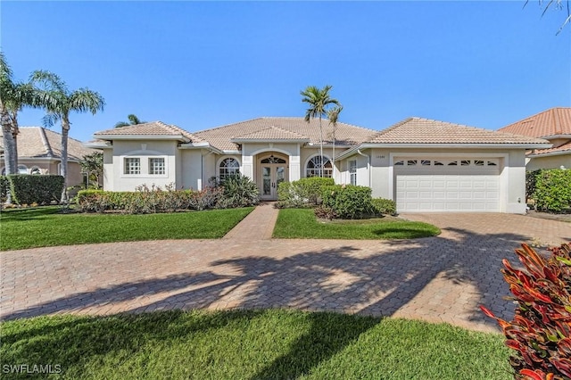 mediterranean / spanish-style house featuring a tile roof, an attached garage, decorative driveway, french doors, and stucco siding