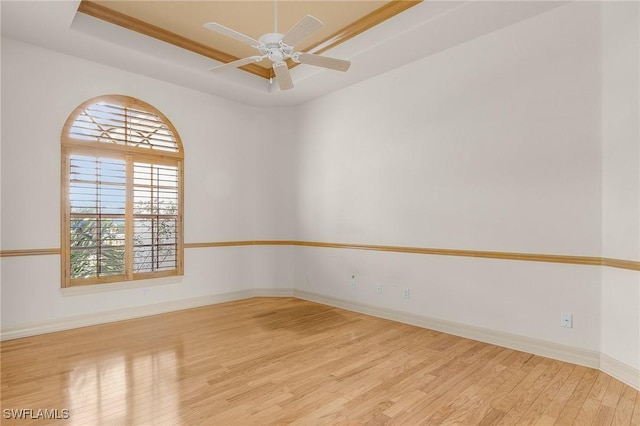 empty room with ceiling fan, wood finished floors, a raised ceiling, and baseboards