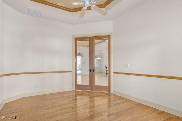 empty room with baseboards, visible vents, wood finished floors, a tray ceiling, and french doors