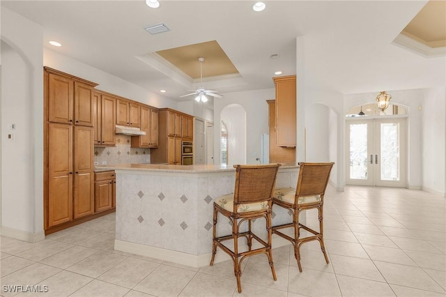 kitchen featuring arched walkways, a raised ceiling, visible vents, light tile patterned flooring, and under cabinet range hood