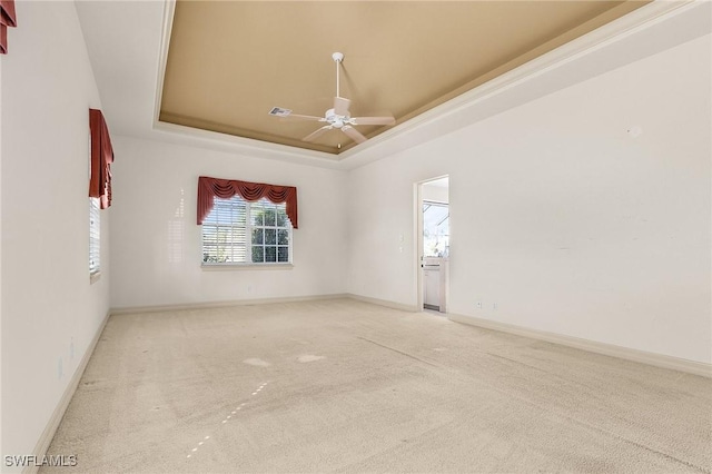 empty room with carpet floors, a tray ceiling, baseboards, and a ceiling fan