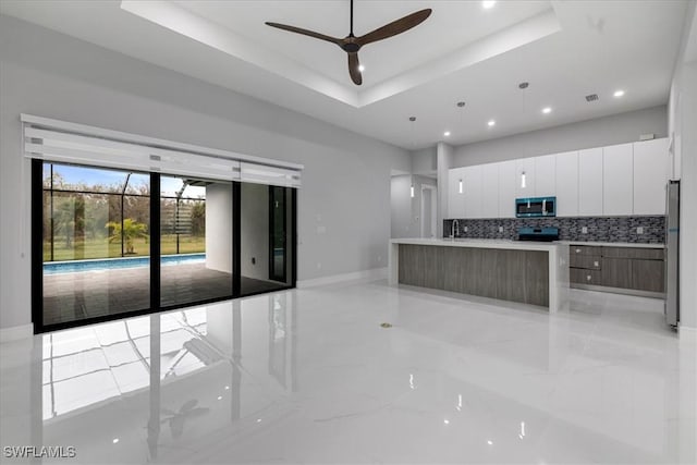 kitchen featuring a spacious island, appliances with stainless steel finishes, white cabinetry, a raised ceiling, and ceiling fan