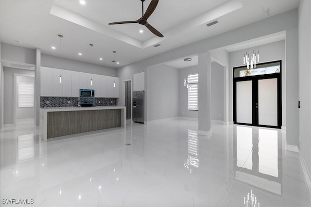 kitchen with a raised ceiling, white cabinets, hanging light fixtures, and a spacious island