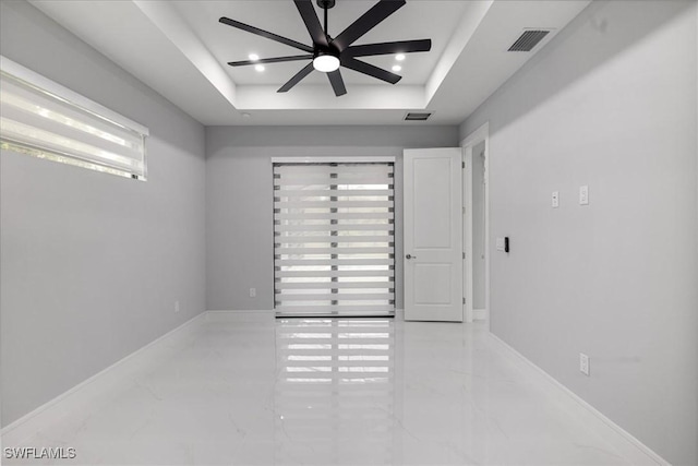 empty room with ceiling fan and a tray ceiling