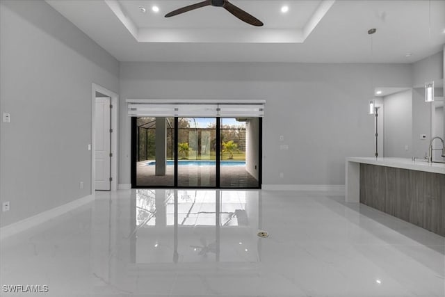 unfurnished living room with ceiling fan, a raised ceiling, and sink