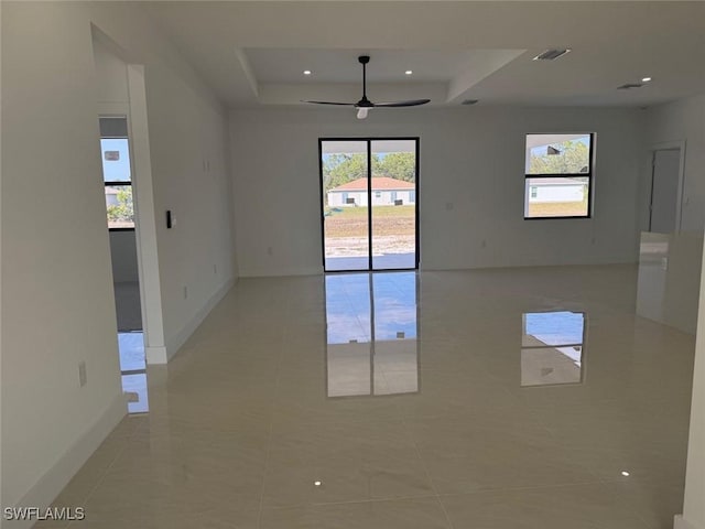 empty room with ceiling fan, light tile patterned flooring, and a tray ceiling