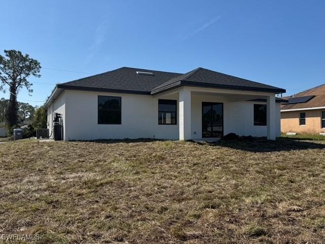 back of property featuring roof with shingles, a lawn, and stucco siding