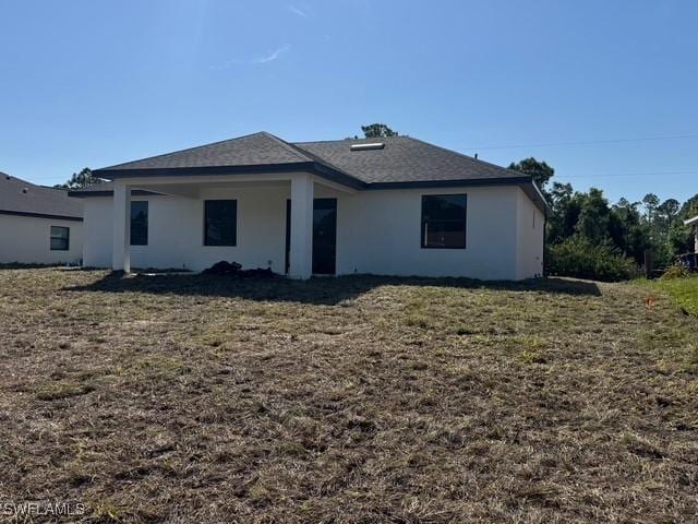 rear view of house featuring roof with shingles, a lawn, and stucco siding