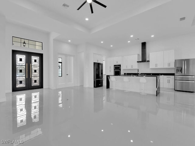 kitchen featuring ceiling fan, wall chimney range hood, a center island, black appliances, and white cabinets