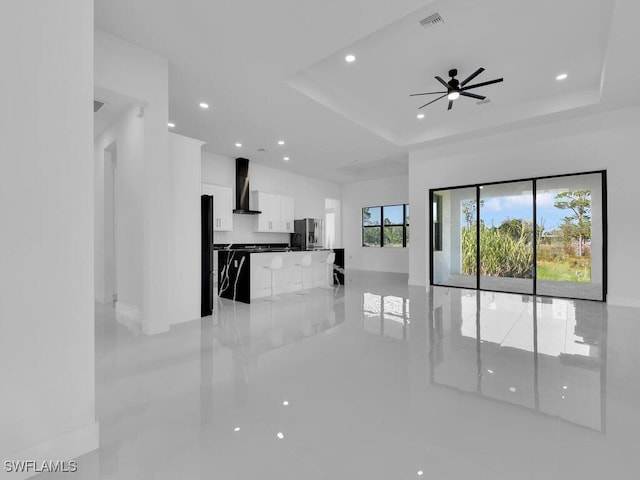 unfurnished living room featuring a raised ceiling and ceiling fan