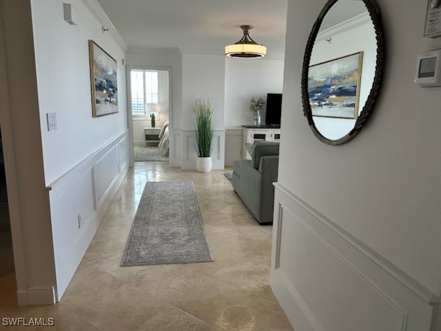 hallway featuring wainscoting, crown molding, and a decorative wall