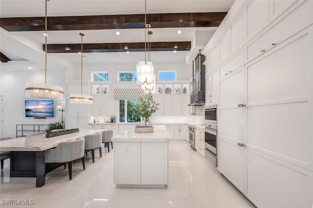 kitchen featuring white cabinetry, wall chimney range hood, a chandelier, pendant lighting, and a center island