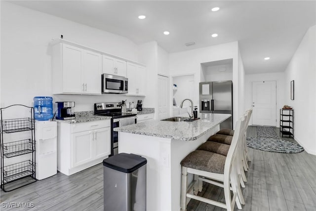 kitchen with appliances with stainless steel finishes, a kitchen island with sink, a kitchen breakfast bar, white cabinets, and sink