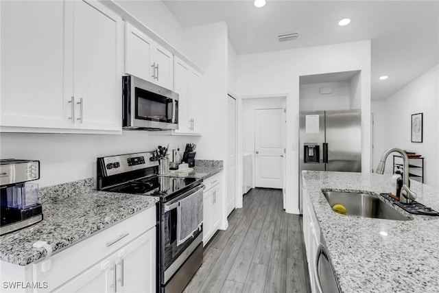 kitchen featuring sink, light hardwood / wood-style flooring, light stone countertops, appliances with stainless steel finishes, and white cabinets