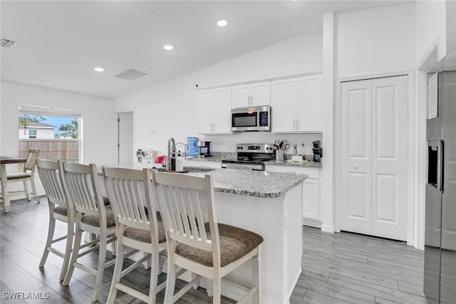 kitchen with a kitchen bar, white cabinetry, appliances with stainless steel finishes, and a kitchen island with sink