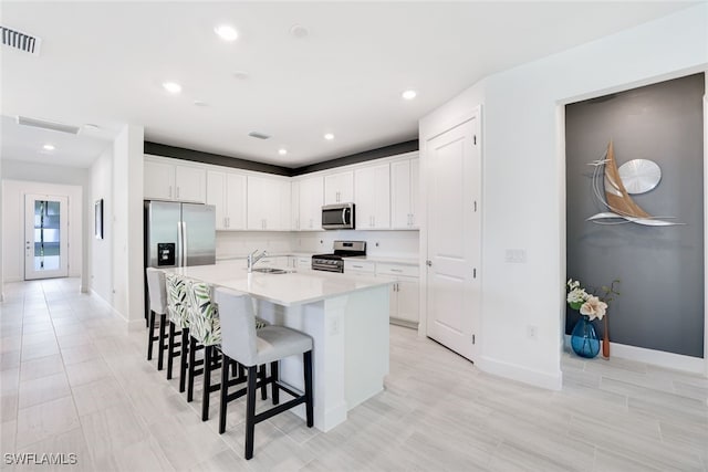 kitchen with an island with sink, a breakfast bar area, stainless steel appliances, white cabinets, and sink