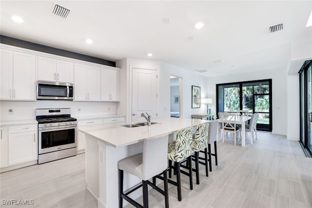 kitchen with white cabinets, appliances with stainless steel finishes, a center island with sink, and sink