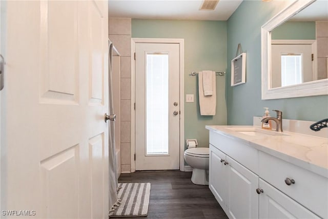 full bathroom with toilet, a healthy amount of sunlight, hardwood / wood-style floors, and vanity