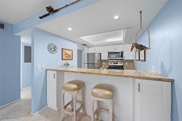 kitchen featuring light stone counters, a peninsula, a tray ceiling, stainless steel appliances, and white cabinetry