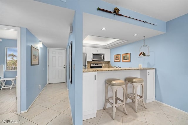 kitchen with appliances with stainless steel finishes, a kitchen breakfast bar, a peninsula, light stone countertops, and white cabinetry