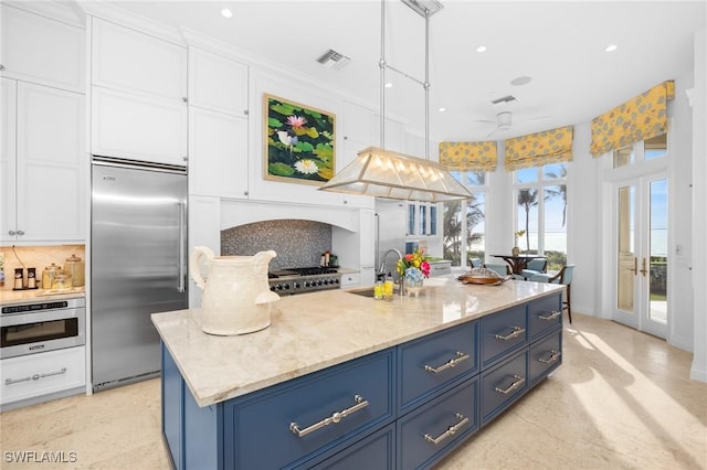 kitchen with tasteful backsplash, oven, pendant lighting, a kitchen island with sink, and built in refrigerator