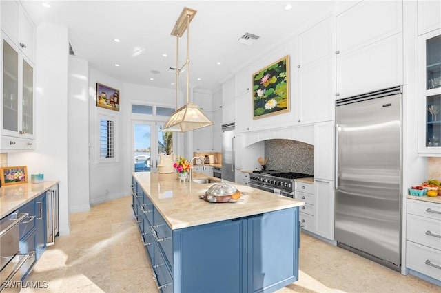 kitchen featuring premium appliances, decorative backsplash, blue cabinetry, a kitchen island with sink, and pendant lighting