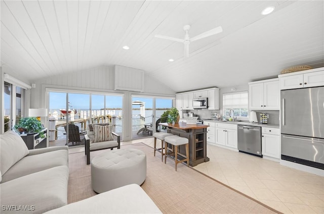 living room featuring ceiling fan, vaulted ceiling, sink, a water view, and light tile patterned floors