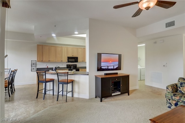 kitchen with ceiling fan, black appliances, a kitchen breakfast bar, light brown cabinets, and light carpet