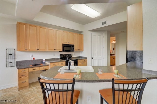 kitchen featuring black appliances, light brown cabinetry, a kitchen breakfast bar, sink, and kitchen peninsula